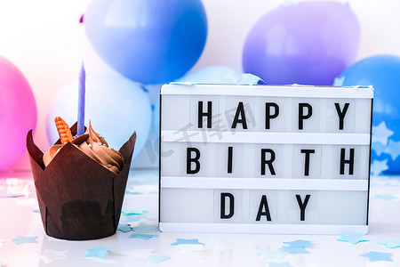 陈皮灯箱摄影照片_带有文字“生日快乐”的灯箱和抽象的离焦模糊节日背景上的巧克力蛋糕蜡烛。