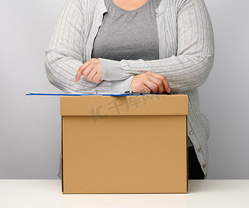 一个穿着灰色衣服的女人站在一个棕色的盒子旁边。