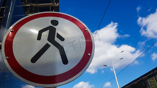 一个白色和红色的圆形路标，中间是一个黑人，在蓝天白云的映衬下禁止行人通行。