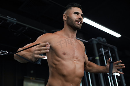 抱胸的男人摄影照片_健康和肌肉发达的男人在健身房的块模拟器上训练胸肌。