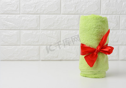 在浴室的白色架子上卷起用红色丝带绑着的特里绿色毛巾