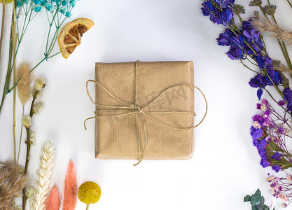 用环保工艺纸包裹的礼品盒，周围环绕着五颜六色的鲜干花顶视图、春天、母亲节、生日、白色背景中突显的贺卡、平躺式现代设计