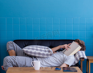 睡觉书摄影照片_男人睡在旧沙发上，脸上盖着书，因为