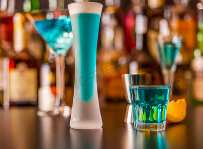 蓝色饮料摄影照片_流行的蓝色饮料在酒吧的背景上用瓶子射击 kamikaze，这是一种清爽的饮料