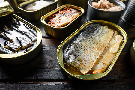 鲱鱼罐头和不同种类的鱼和海鲜，在质朴的深色木板侧视图上。