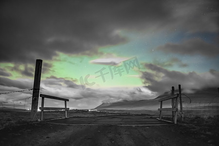 云层上摄影照片_冰岛北极光的北极光透过冰岛农场大门上的云层缝隙照耀着黑白和绿色
