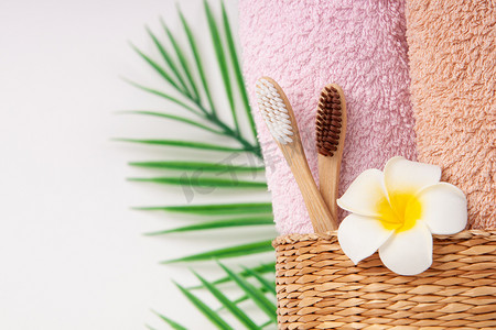 竹牙刷，柳条木篮里有毛巾，棕榈叶和鸡蛋花，白色背景上有复制空间。