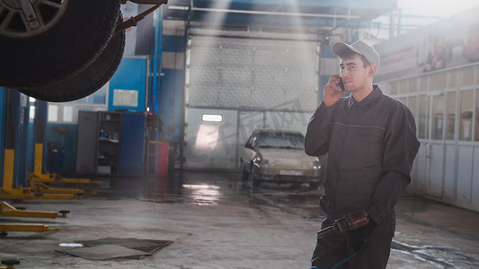细胞防护摄影照片_车库汽车服务 — 举起的汽车附近的一名机械师用手机讲话，广角