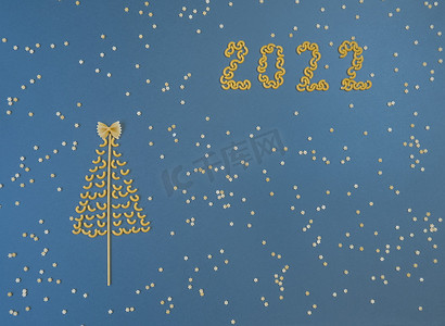 圣诞树上排列着干意大利面和数字 2022，蓝纸背景上还有意大利面的星星。