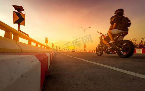 黄色曲线交通标志上的太阳能电池板能量和曲线道路上骑摩托车的骑自行车的人的运动模糊。