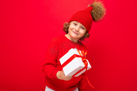 一个红墙背景卷发的酷男孩，穿着毛衣，手里拿着圣诞树，手里拿着礼盒