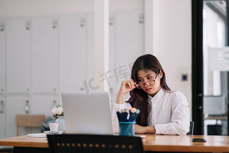 照片中，美丽的亚洲女商人足智多谋，戴着眼镜，严肃地看着笔记本电脑，在家办公室观看在线培训。