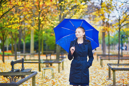 巴黎卢森堡花园秋春雨天带蓝伞的年轻女子