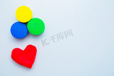 照片上方是一颗用红色面团做成的心形模型，底部是白色背景的黄色、绿色和蓝色圆圈。
