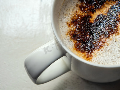 柔软的食物摄影照片_咖啡杯中柔软的白色牛奶泡沫和洒在上面的咖啡粉的深棕色