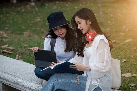 两个学生坐在公园里看书和交流。
