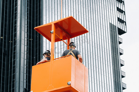 建筑摇篮里的工人爬上起重机到一座大型玻璃建筑。起重机将工人抬到汽车座椅上。建筑