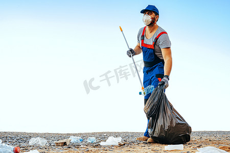 收集垃圾摄影照片_男子志愿者用伸展杆在海滩上收集垃圾
