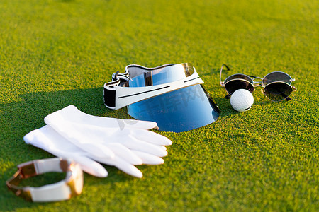 躺在绿色高尔夫球草上的豪华高尔夫设备白手套太阳镜看球太阳帽