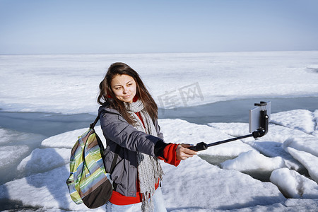 户外冰冷风景中的女性旅行者使用独脚架自拍照片
