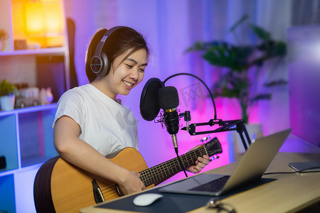 嘻哈熊猫字体摄影照片_美丽的女孩用耳机唱歌，在家庭录音室用麦克风弹吉他录制新歌