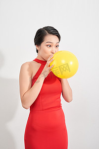 身穿红色衣服的快乐、情绪化的亚洲年轻女性正在工作室里吹黄色气球。