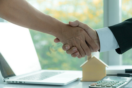 房地产经纪人在签订购房合同后坐在办公桌前与客户握手。