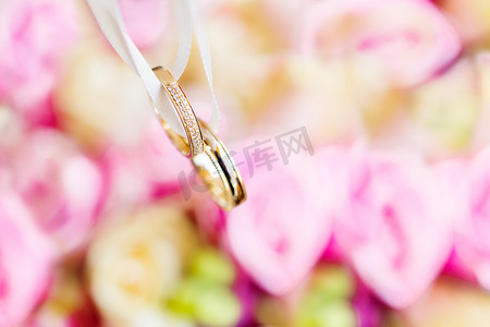 新娘花束上的金色结婚戒指，上面有粉色和黄色的玫瑰。