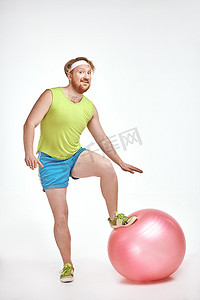 红头发、留胡子、丰满的男人把他的腿放在健身球上