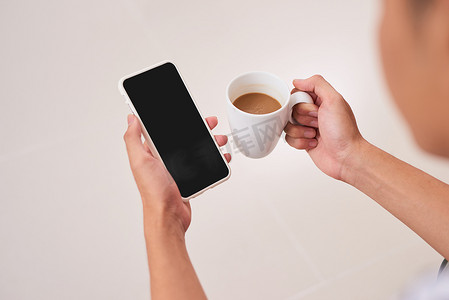 拿苹果手机的手摄影照片_在现代阁楼咖啡馆喝咖啡时，女性双手拿着带有空白黑屏的白色手机的模型图像