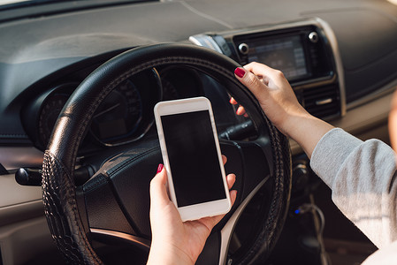 女性手在驾驶汽车和离开家时使用带有空白屏幕的移动智能手机的样机图像。