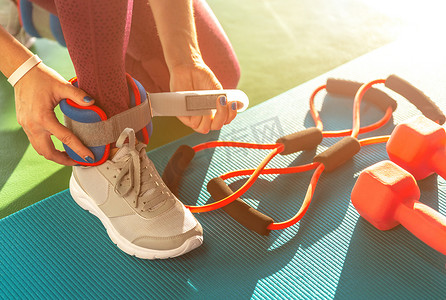 女人在健身房开始锻炼前先戴上脚踝重量，在垫子上用哑铃锻炼健康和健身概念