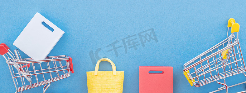 抽象设计元素，年度销售概念，购物季节-迷你黄色购物车，带纸袋，隔离在柔和的蓝色背景，顶视图，平躺。