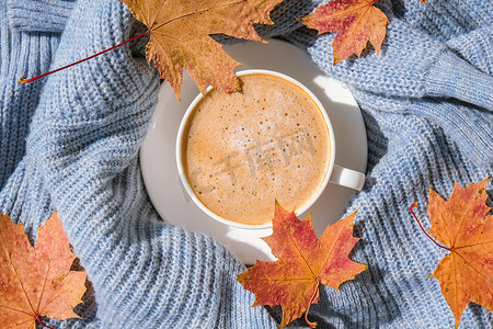 蓝色针织毛衣上的白色早晨暖咖啡，枫叶黄叶背景。