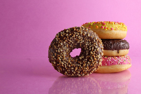 甜蜜的静物甜甜圈柏林特写镜头在后面躺着一堆三个甜甜圈巧克力粉红色黄色在明亮的粉红色紫红色背景上，有一个文本位置，还有一个用于咖啡馆的 cpixpe，用于放置胶水的桌布