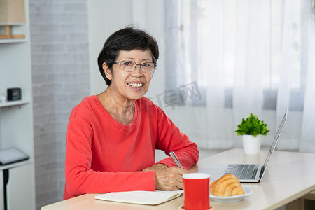 室内家居平面摄影照片_坐在桌子上使用笔记本电脑放松的高级亚洲女性。
