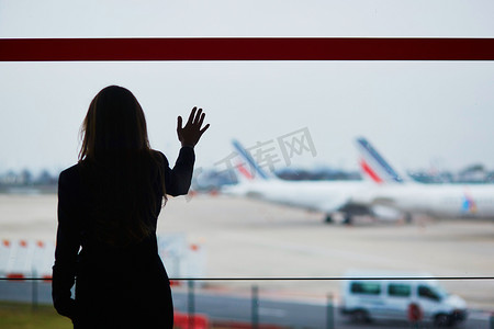 手提行李摄影照片_国际机场提着手提行李的女人，透过窗户看飞机