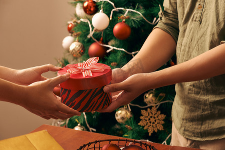 特写亚洲年轻男子在家里的沙发和圣诞树背景上拿着圣诞红色礼盒