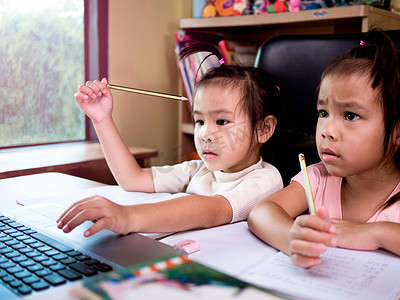 两个小女学生在家里的在线课程中学习数学作业，在冠状病毒爆发期间保持社交距离。
