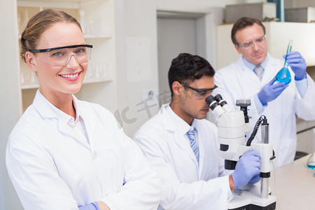 看显微镜摄影照片_同事们用显微镜工作时，科学家微笑着看着相机