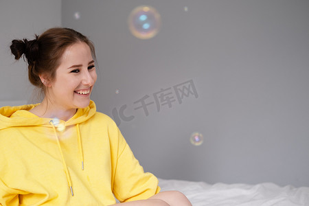 肥皂泡泡摄影照片_黄色迷人的年轻女子的画像，在明亮的灰色背景上的肥皂泡泡中。
