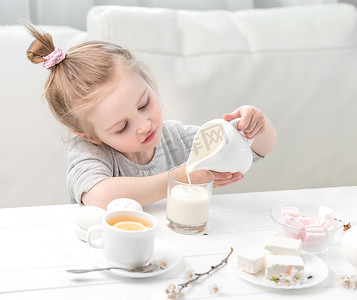小女孩往她的茶杯里倒牛奶