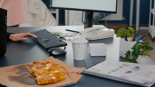 坐在电脑前办公桌前吃披萨片的女商人的特写