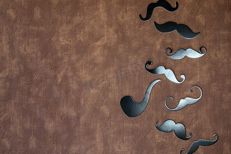 棕色皮革背景纹理上的黑色胡须和帽子，带有复制空间、国际男士节和父亲节概念