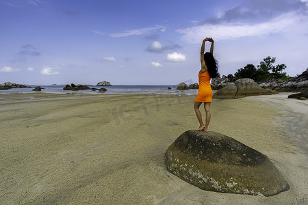 云洞摄影照片_穿着橙色裙子站在大石头上的女人