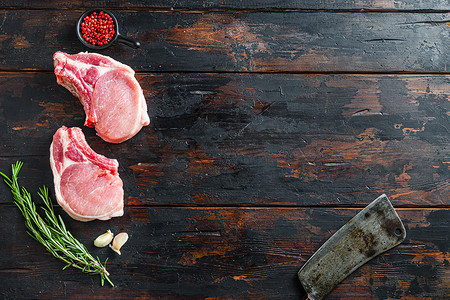 文字猪摄影照片_生猪肉排配香草和香料，配上肉美式切肉刀，在深色质朴的木质背景侧视图空间上放置文字。