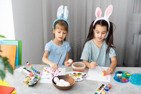 彩绘蛋摄影照片_两个快乐可爱的女孩姐妹画复活节彩蛋，哦笑，展示彩蛋和彩绘手