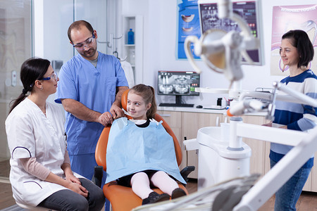 小女孩穿着牙科围兜坐在牙医办公室的椅子上