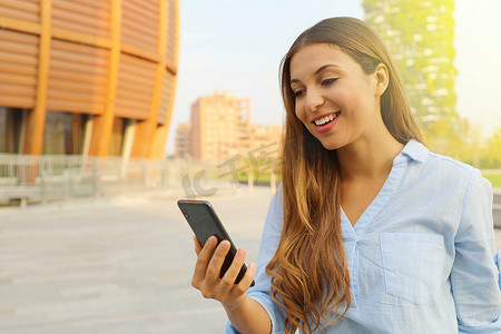 在意大利米兰阳光明媚的日子里，年轻女子在智能手机上打视频电话或发短信，走在街上。