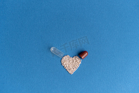 颗粒从心形胶囊中倾倒在经典的蓝色背景上。